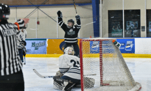 Goal being score at a hockey game with the referee signaling the goal, the goalie pads down, and the hockey player's arm up in celebration